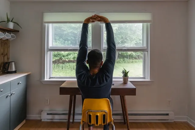 A man stretching while working at his desk.