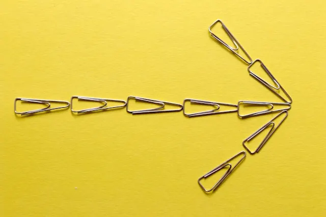 Silver paper clips forming an arrow on yellow surface.