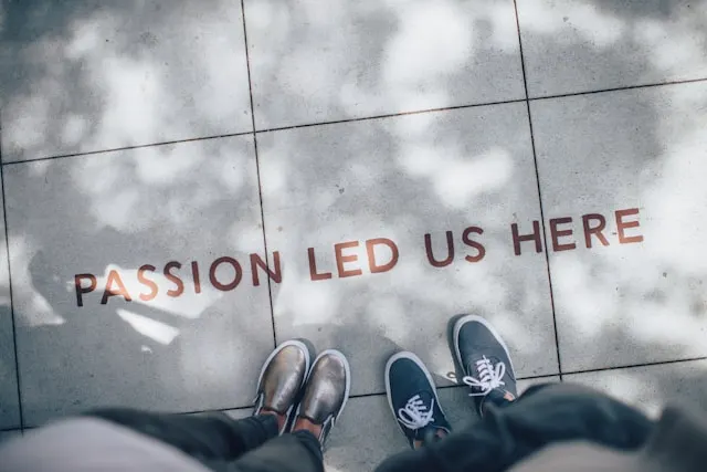 Two people standing on a gray floor with “Passion Led Us Here” written on it.