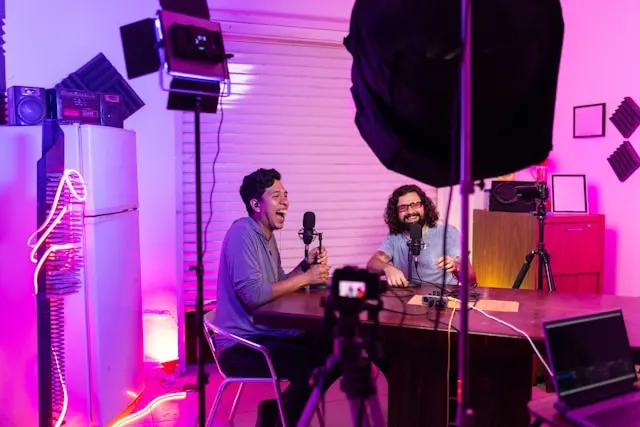 Two men in a pink and purple video podcast studio setup.