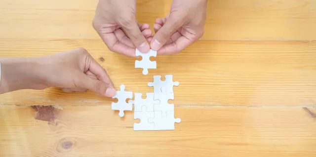 Top view shot of hands assembling a jigsaw puzzle, representing collaboration in a Level 10 meeting