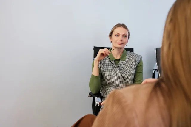 A woman sitting on a chair and attentively listening to another person.