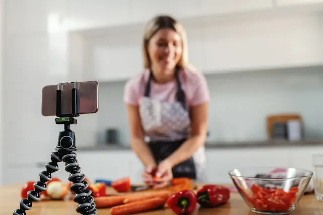 A woman shooting a video while chopping vegetables in a kitchen.