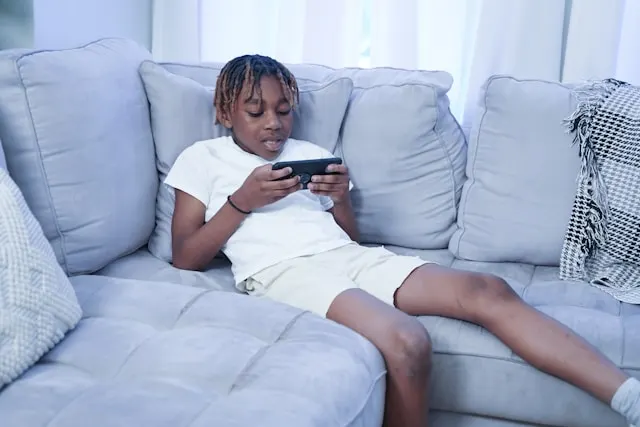 A boy laying on a couch and looking at a smartphone.