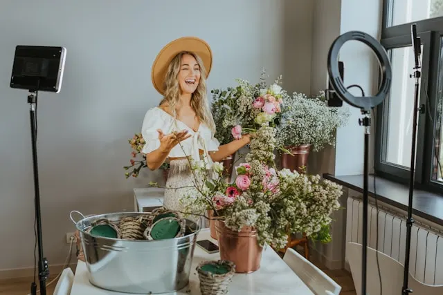 A woman standing in front of a table with flowers while talking to a camera.