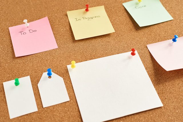 Three paper notes with words "To Do", "In Progress", and "Done" pinned to a cork board.