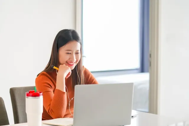 A woman smiling while looking at her laptop screen.