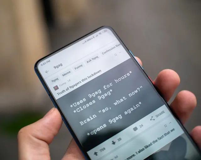 Person holding a smartphone displaying a 9GAG meme.