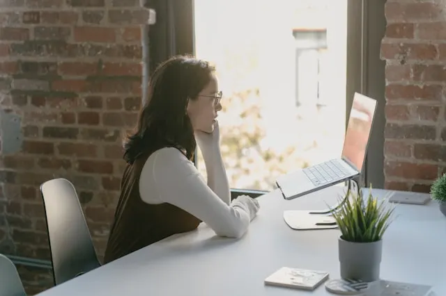 A woman sitting at a table and looking at her laptop.