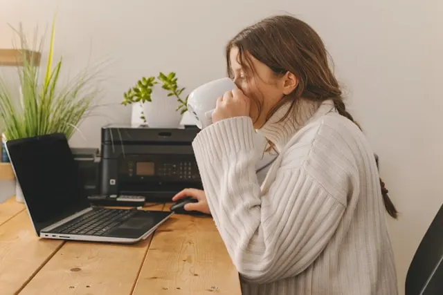 A woman working on her laptop while drinking a beverage from a mug.