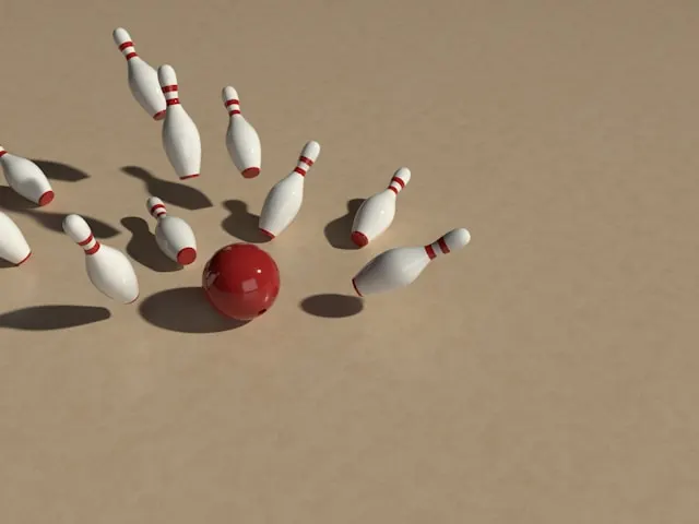 A group of bowling pins hit by a red bowling ball.