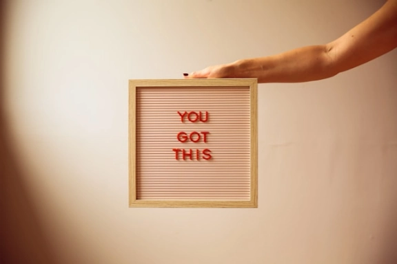 A hand holding a sign that says you got this.