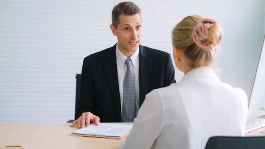 Two people sitting at a desk and talking during a job interview.