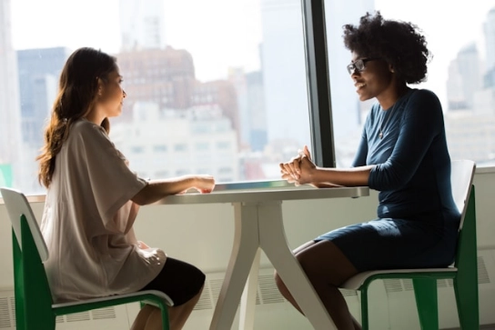 Two women sitting at a table practicing for an interview.