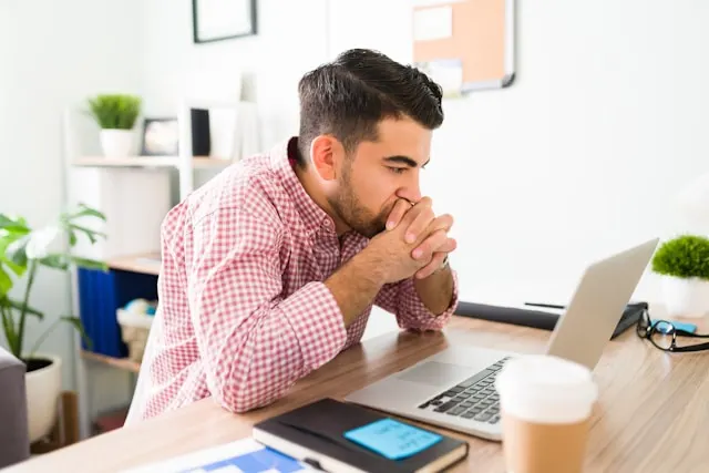 A man staring at his laptop screen while working at his desk.